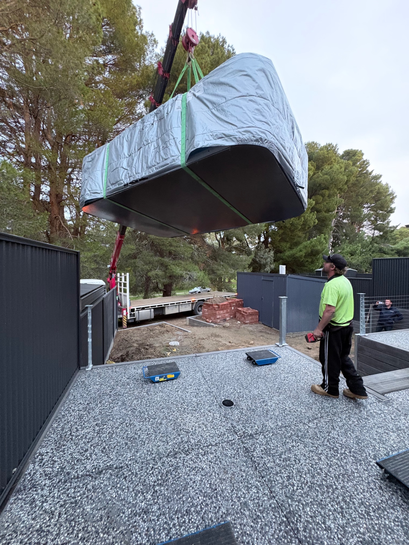Crane lifting a new spa over the fence into a backyard